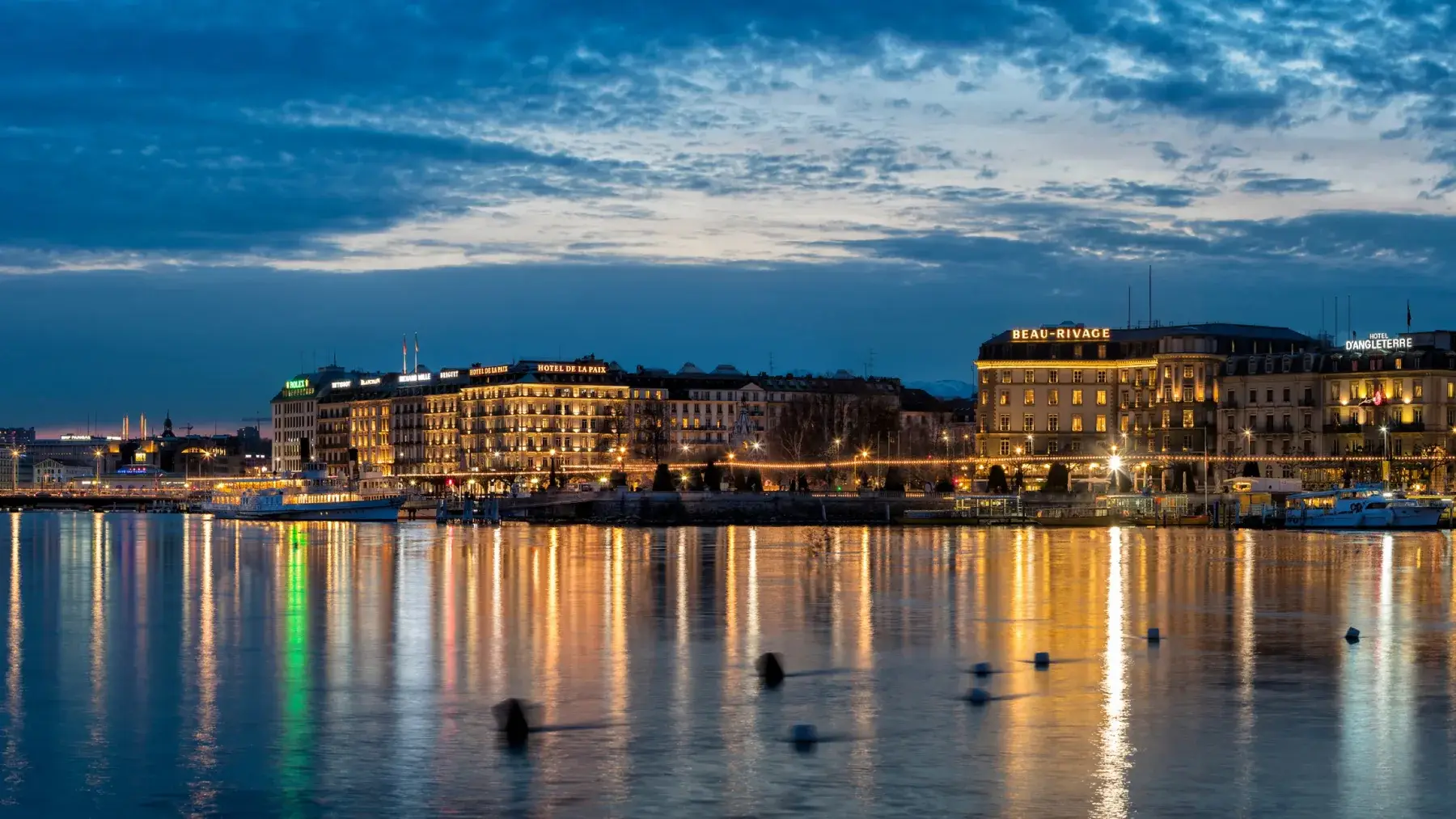 La rade de Genève au crépuscule, les hôtels du quai du Mont-Blanc illuminés se reflétant dans le lac Léman