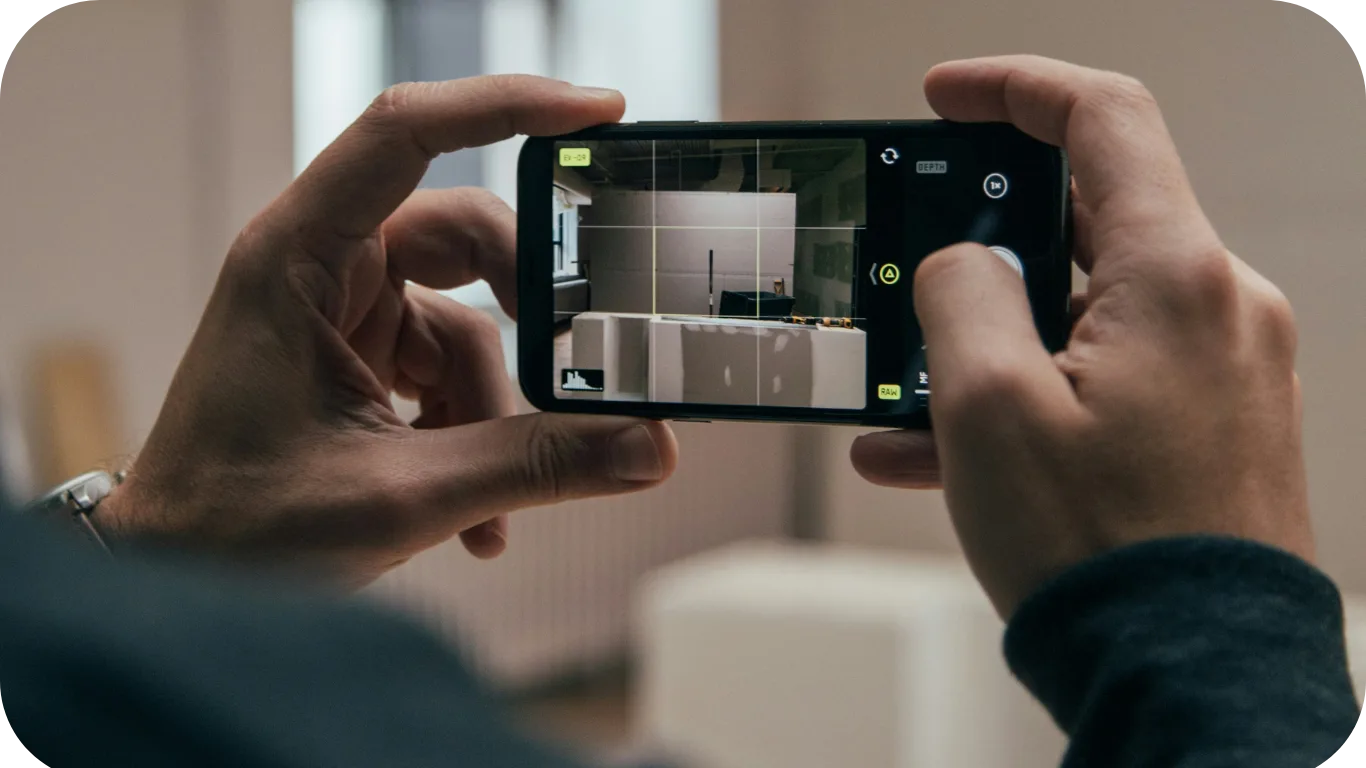 Mains tenant un smartphone à l'horizontale pour photographier un intérieur, grille de cadrage affichée à l'écran