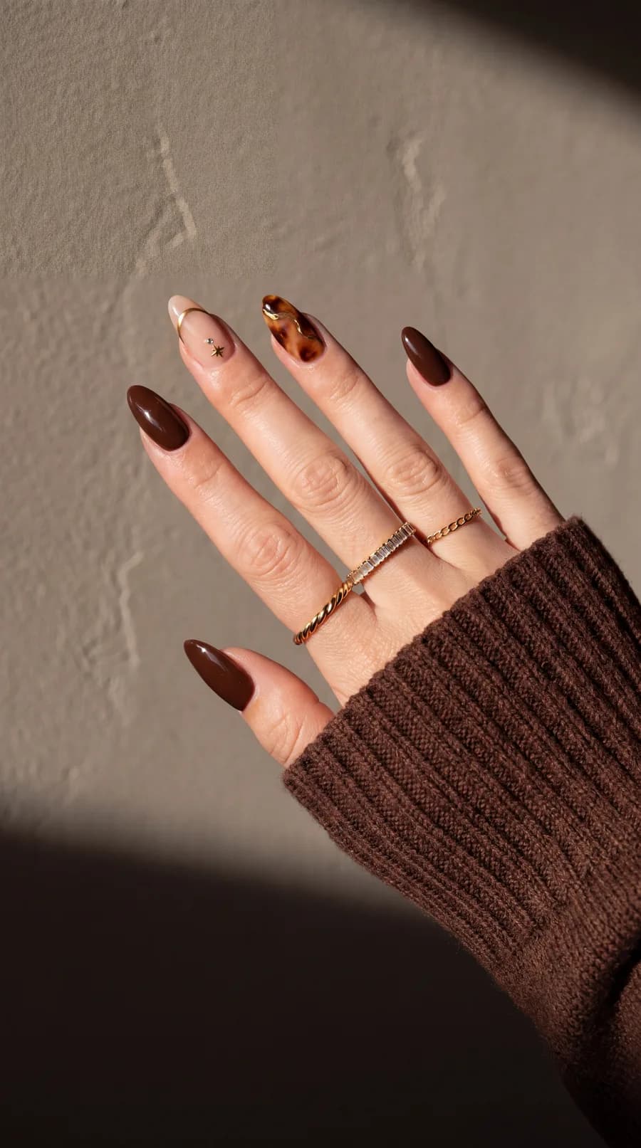 Main aux ongles amande brun chocolat, rehaussés de fins liserés dorés