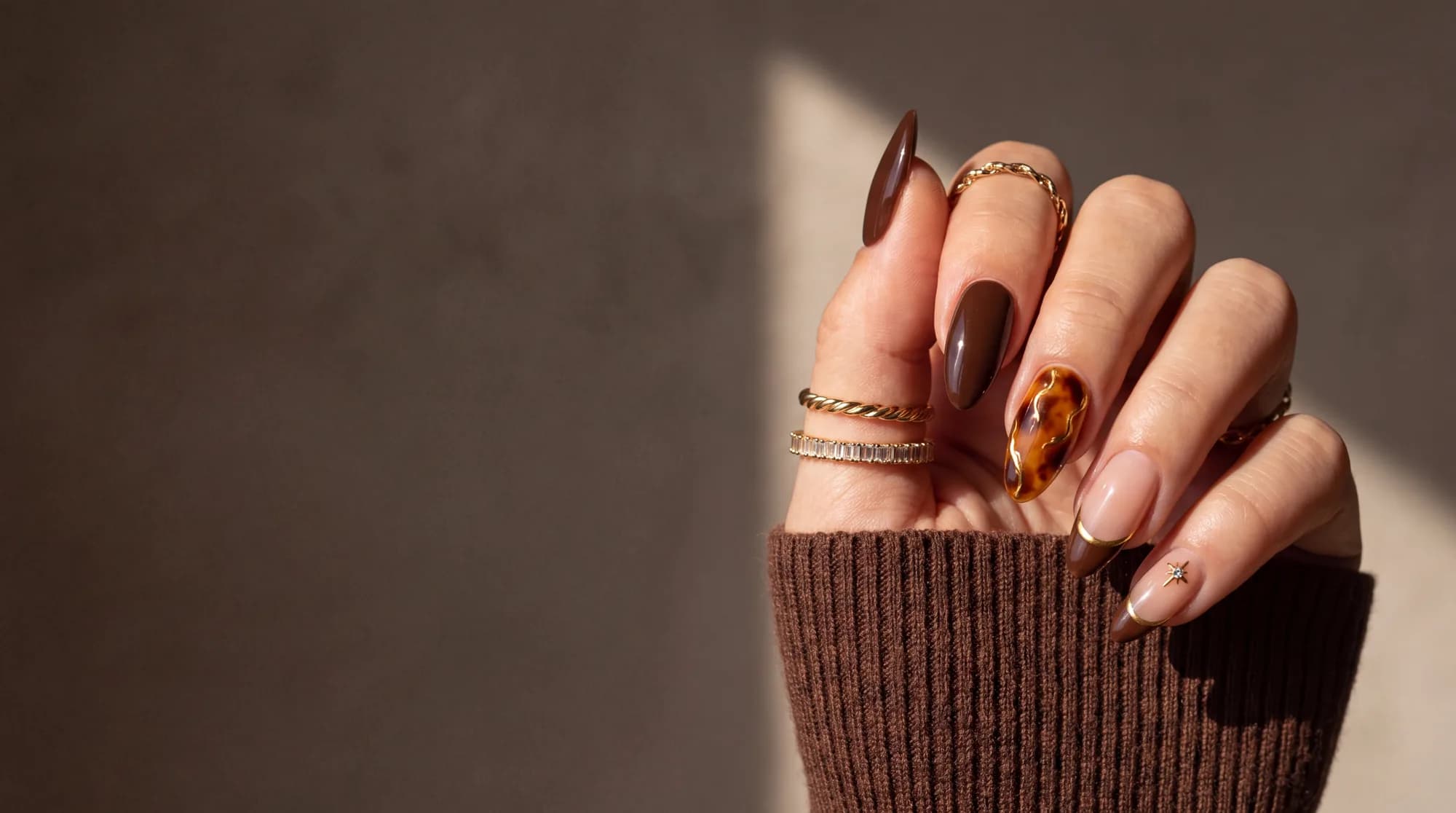 Main aux ongles amande brun chocolat, rehaussés de fins liserés dorés